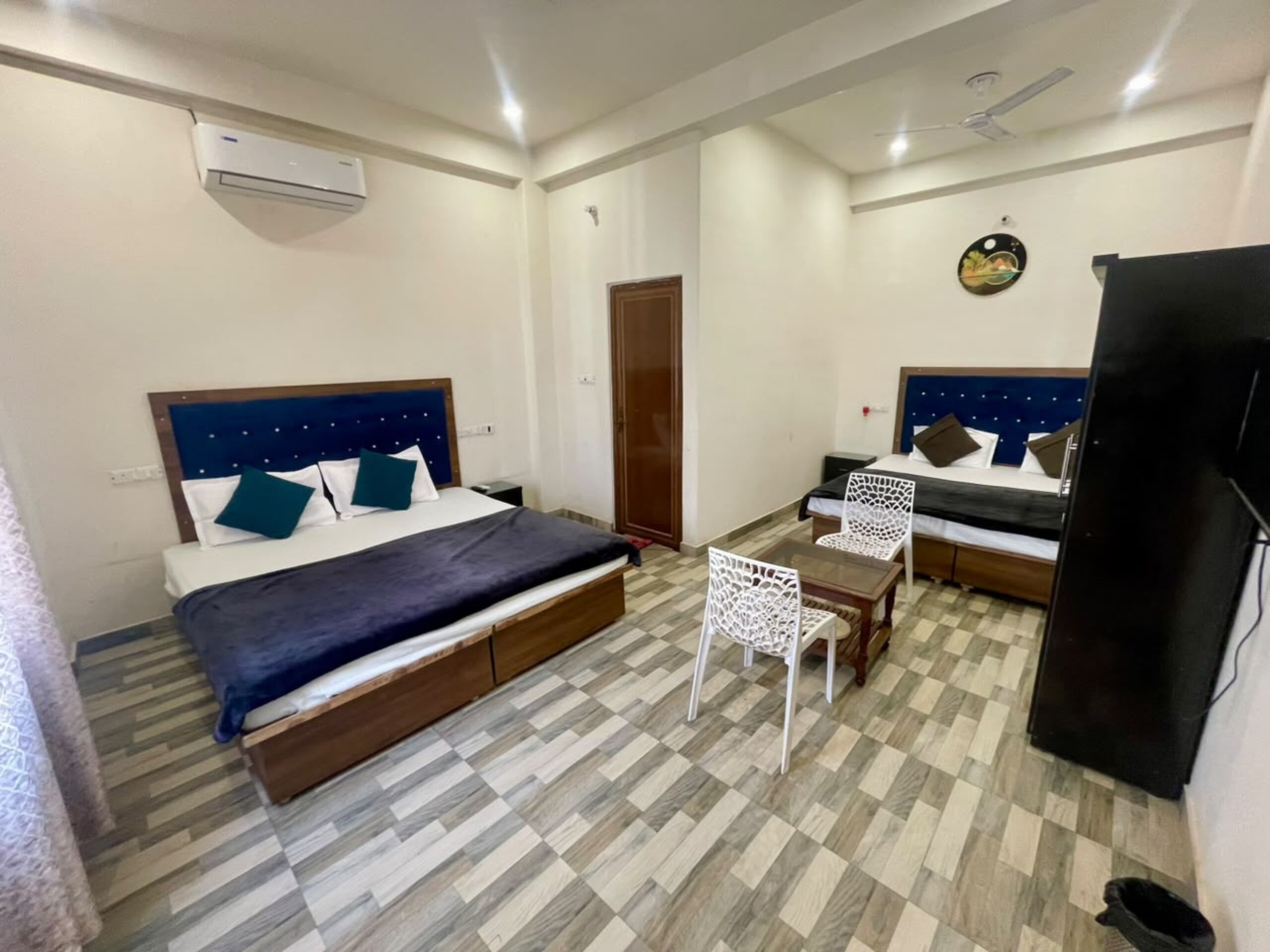 Una habitación de hotel con cama, escritorio, dos sillas, televisor y aire acondicionado.