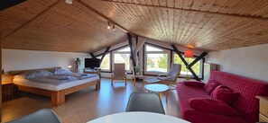 Une pièce avec un plafond en bois, un lit, un canapé rouge, une télévision et une fenêtre.