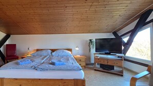 A bedroom with a wooden ceiling, a bed with checkered bedding, a TV on a wooden stand, and a window with a view. - Vacation apartment FR1 - "Seewohnung" - Holiday apartment "Seewohnung" with (Graal-Müritz)
