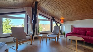A room with a wooden ceiling, large windows, a red sofa, two chairs, and a small table. - Vacation apartment FR1 - "Seewohnung" - Holiday apartment "Seewohnung" with (Graal-Müritz)