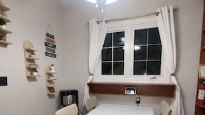 Un comedor con una mesa blanca, sillas de madera, un ventanal con cortinas blancas y estantes empotrados decorados con objetos.
