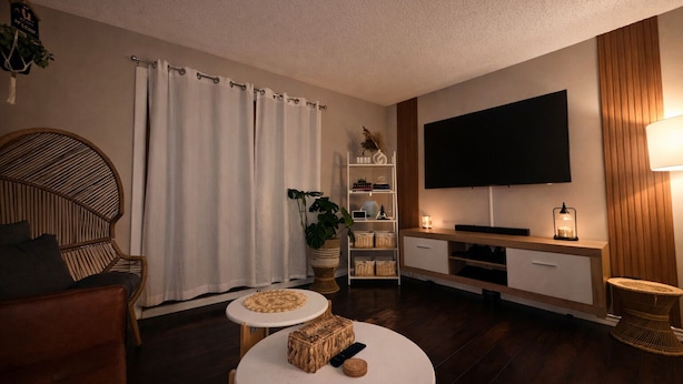 Una sala de estar con un sofá, una mesa de centro redonda, un televisor, una estantería y una lámpara.