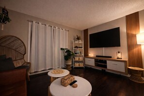 Un salon avec un canapé, une table basse ronde, un téléviseur, une bibliothèque et une lampe.
