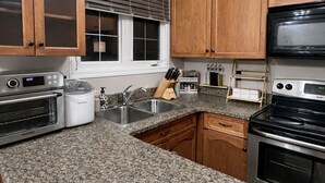 Una cocina con encimeras de granito, armarios de madera, estufa, horno, microondas y un ventanal con persianas.