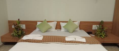 A hotel room with a bed, pillows, a nightstand, a wall with artwork, and a flower arrangement.
