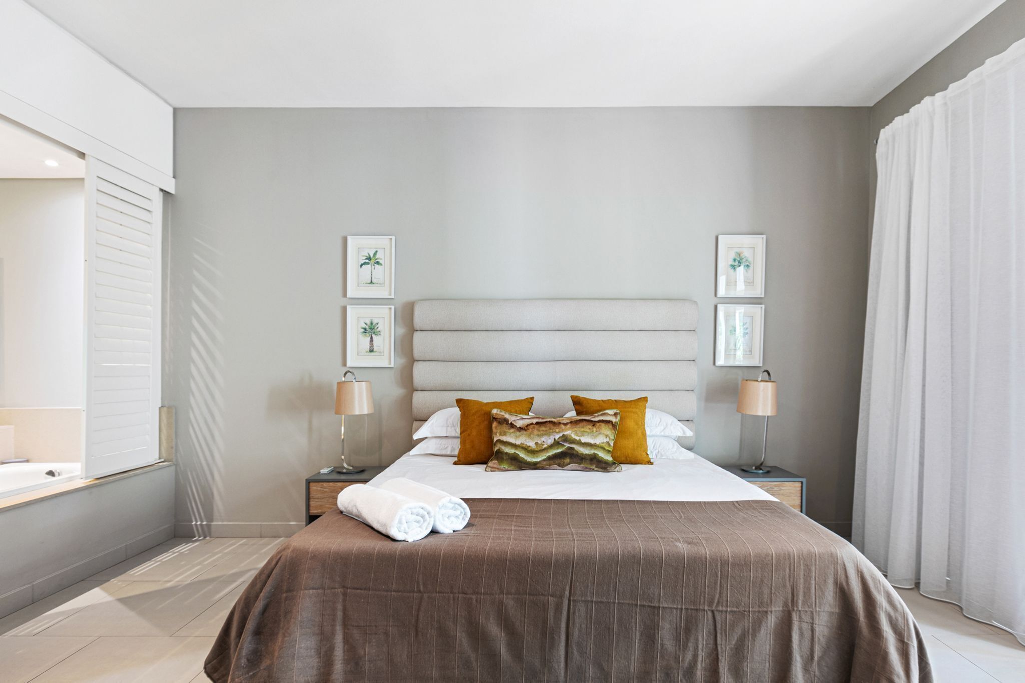 A hotel room with a bed, two bedside tables, a nightstand, a lamp, and framed pictures on the wall.