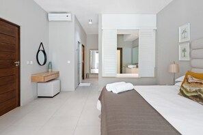Ein modernes Hotelzimmer mit einem Bett, einem Schminktisch mit Spiegel, einer Holztür und einem Flur, der zum Badezimmer führt.