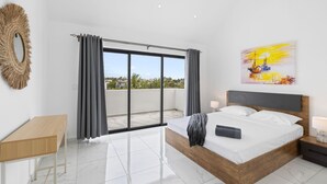 A modern bedroom with a large bed, a wooden desk, and a view of the city through a sliding glass door. - 7 Green Village - Three Bedroom Apartment, Sleeps 6 (Grand Baie)