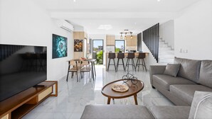 A modern living room with a flat-screen TV, a sofa, a coffee table, and a dining area with chairs and a table. - 7 Green Village - Three Bedroom Apartment, Sleeps 6 (Grand Baie)