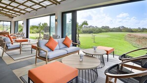 Un espace intérieur moderne, doté de grandes fenêtres, d’un canapé avec des coussins orange et offrant une vue sur un terrain de golf.