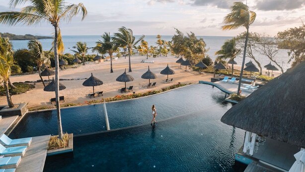 Un espace piscine offrant une vue sur la plage, les palmiers et des chaises longues.