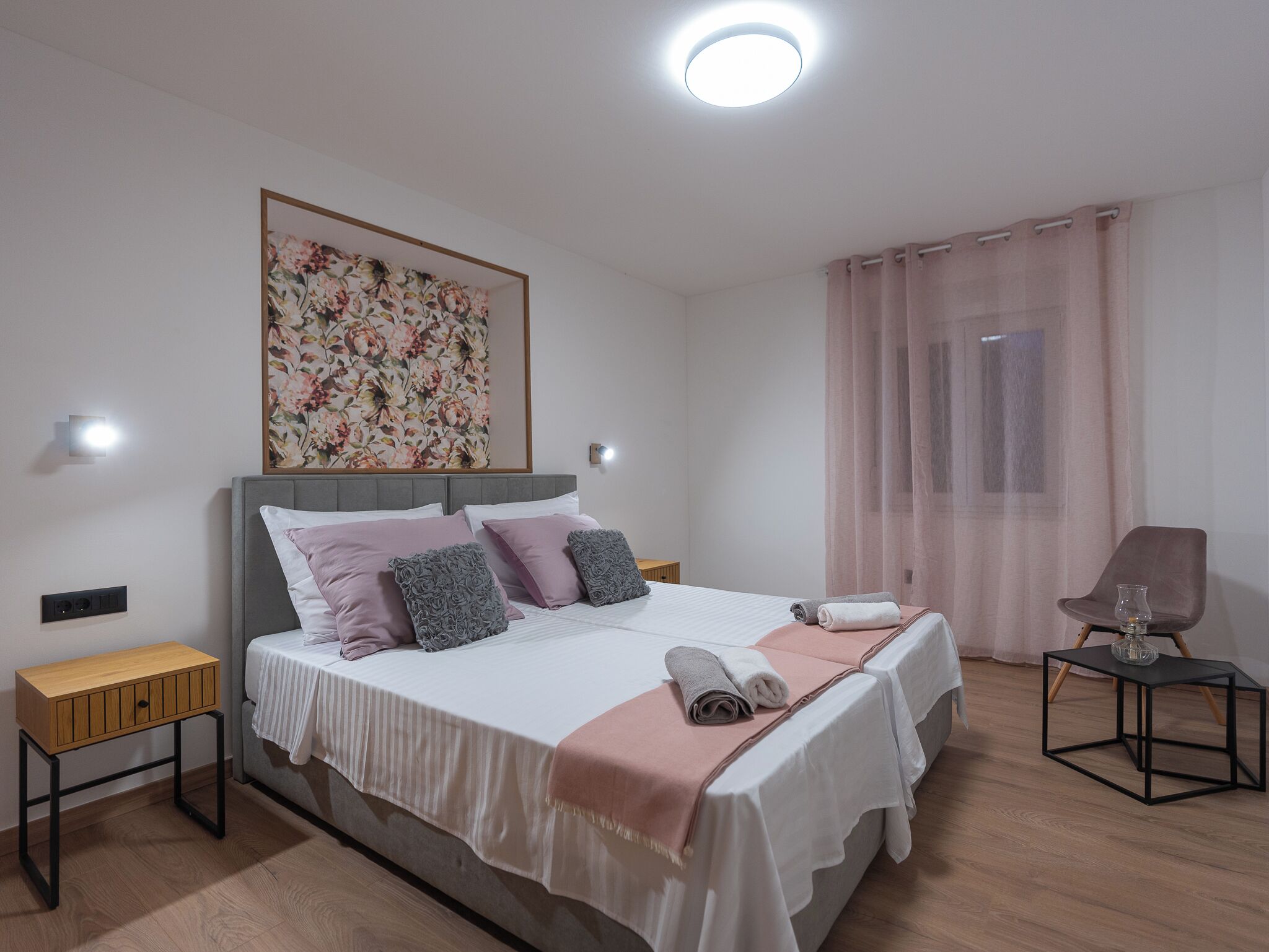 A bedroom with a bed, bedside tables, a chair, a painting, and a window with curtains.