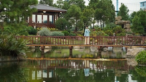 Ein friedlicher Garten mit einem hölzernen Gazebo, einer Brücke und einem Teich, der die Umgebung spiegelt.