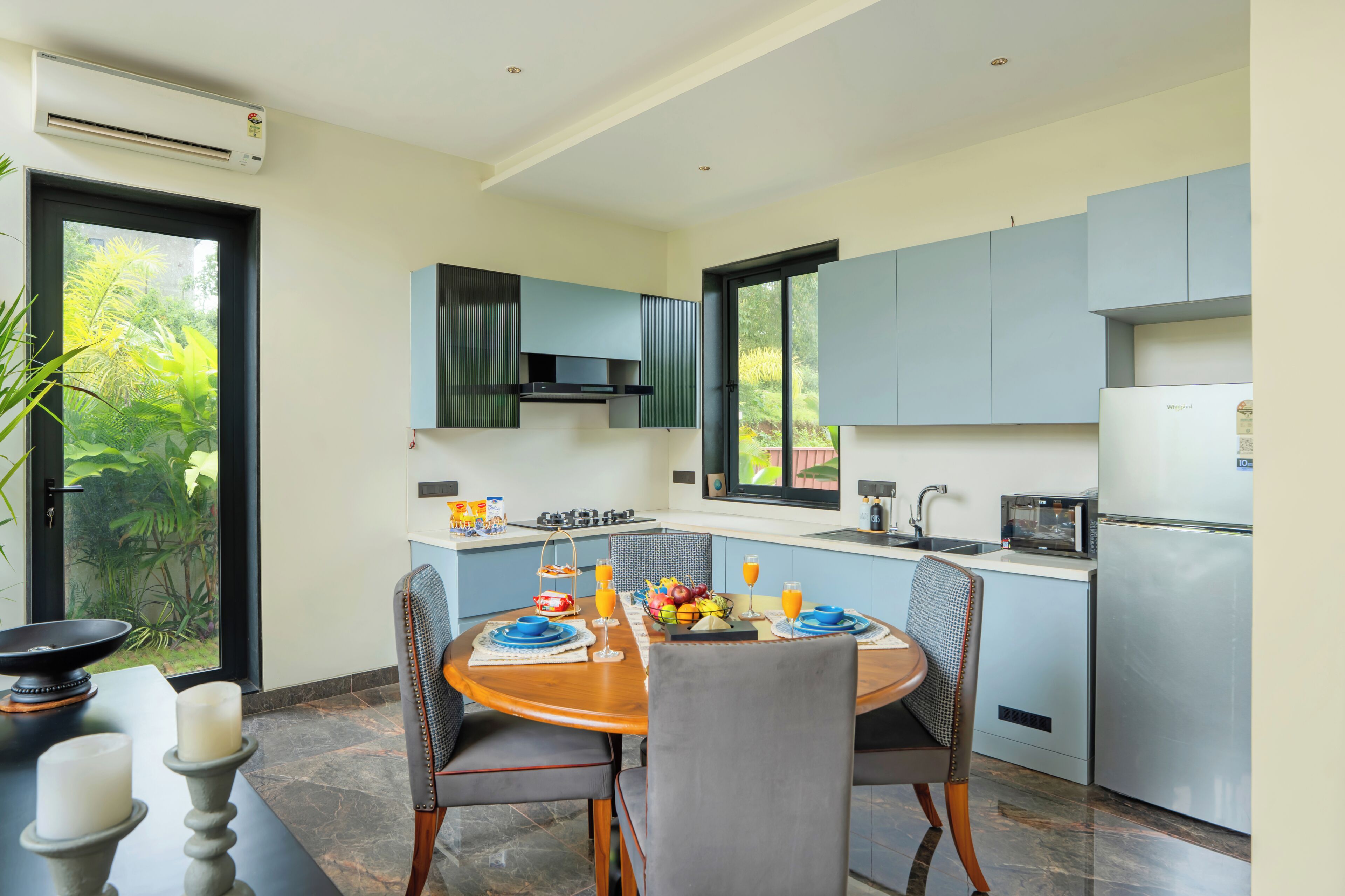 Una cocina moderna con armarios azules, una mesa de comedor dispuesta con platos, vasos y un frutero.