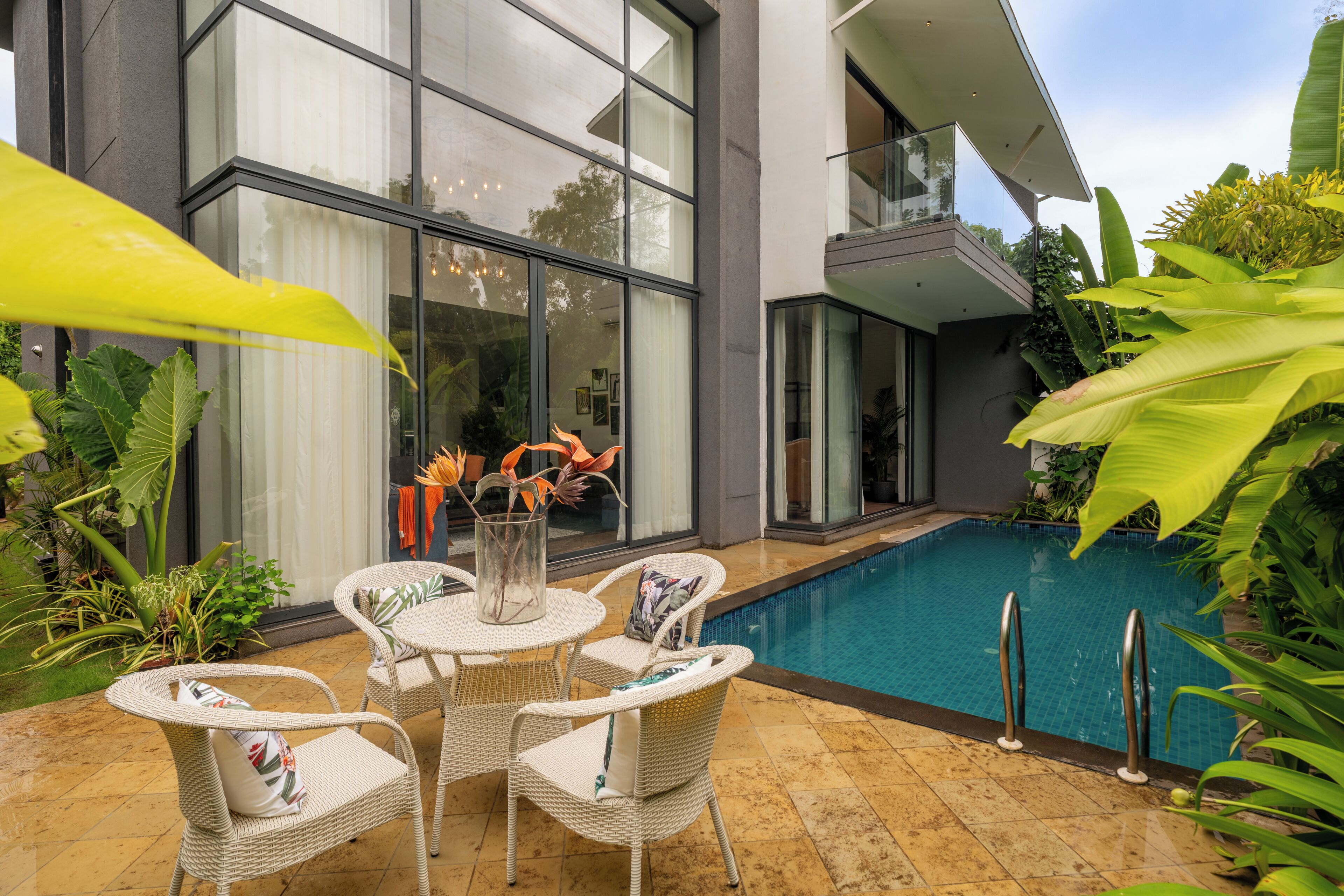 A modern house with a swimming pool, wicker furniture, and tropical plants.