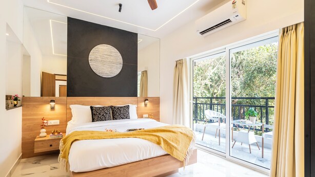 Un dormitorio moderno con una cama grande, un adorno circular en la pared y un balcón con mobiliario exterior.