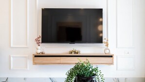 Una sala de estar moderna con un televisor montado, una estantería de madera con objetos decorativos, una planta en maceta y una encimera de mármol.