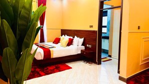 Una camera d'albergo con un letto, un comodino e una pianta grande.