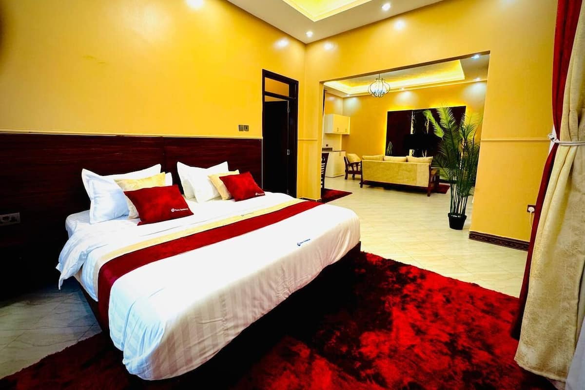 Una habitación de hotel con una cama grande, una alfombra roja y vistas a un comedor.