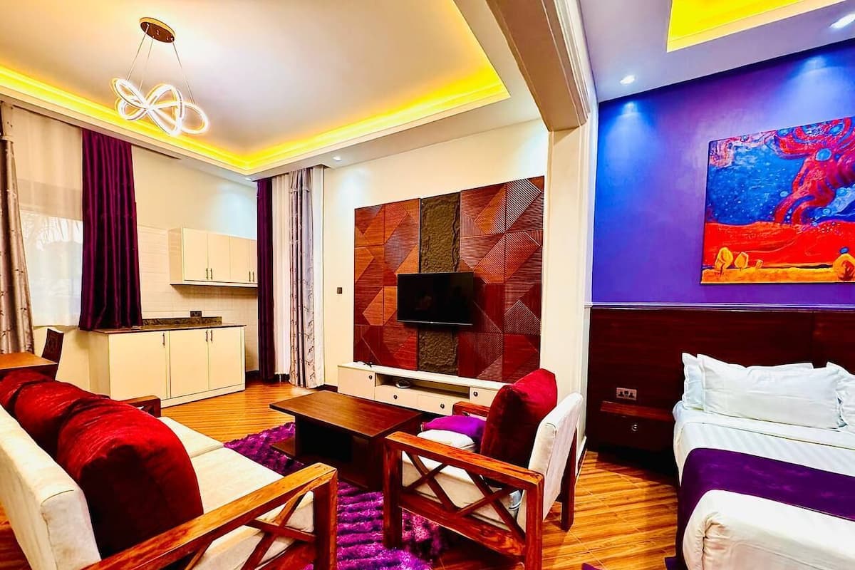 Una habitación de hotel con sofá, cama, televisor, escritorio y un cuadro en la pared.
