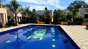 Una piscina con la scritta 'LIFEWATER' sulle piastrelle, circondata da palme e da un edificio con un percorso pedonale in piastrelle.