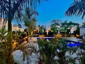 A pool area with palm trees, lounge chairs, and modern buildings in the background. - Pieme Hotel Residence (Kiwenda)