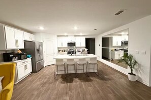 A modern kitchen with white cabinets, a central island with bar stools, stainless steel appliances, and a yellow chair. - Spacious 4BR home near beach and downtown Entire home in St. Augustine, Florida (St. Augustine)
