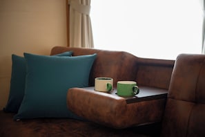 Un sofá de cuero marrón con cojines color turquesa, una mesita y dos tazas.