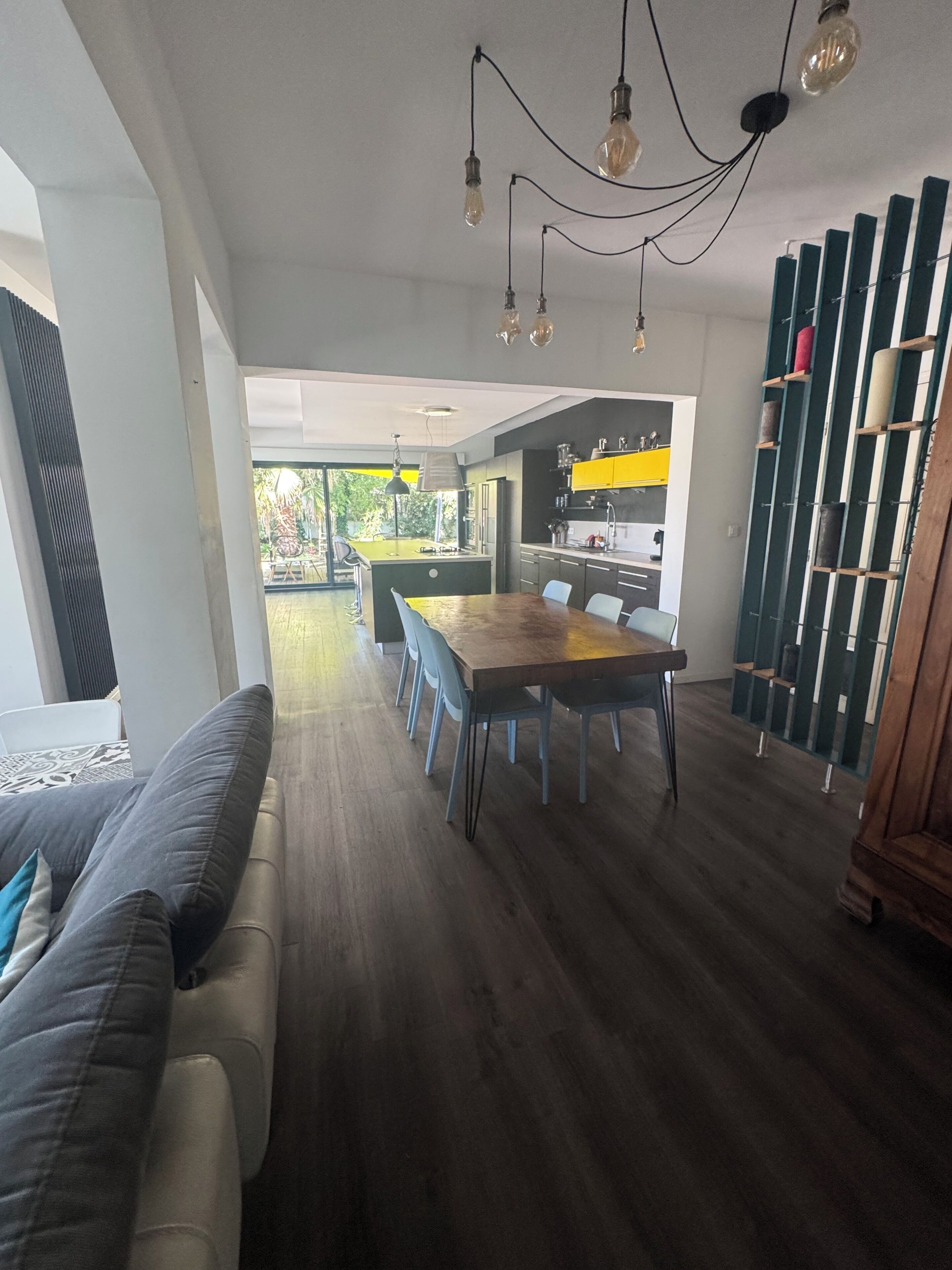 A modern kitchen with a dining area, a sofa, and a view of the outdoors.