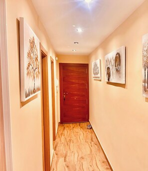 A hallway with wooden flooring, a wooden door at the end, and artwork on the walls. - RUMBO BEACH'S APARTMENT (Almuñecar)