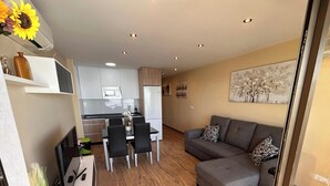 Ein moderner Wohnraum mit Essbereich, Küche und einem grauen Sofa mit gemusterten Kissen.