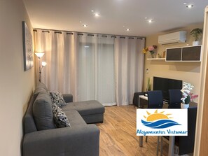 Ein modernes Wohnzimmer mit einer Couch, einem kleinen Tisch, einem Fernseher und einem Schild mit dem Logo 'Alojamientos Vistamar'.