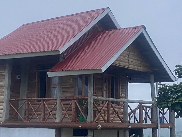 A wooden cabin with a red roof and a balcony with a railing. - Nature Flows Eco-farm Cottage & campsite (Fort Portal)