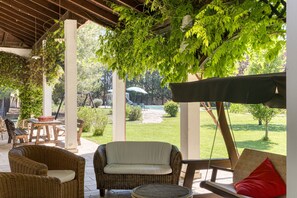 Uma área de terraço externa com móveis de vime, um espaço coberto para sentar e vista para o jardim e piscina.
