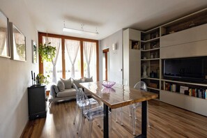 Un espace de vie moderne avec un plancher en bois, une table à manger avec des chaises, un canapé, un téléviseur et une bibliothèque.