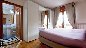 Een slaapkamer met een bed, een kledingkast, een spiegel, een raam met gordijnen en uitzicht op het omliggende landschap.