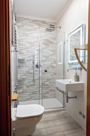 Une salle de bain moderne avec une douche à parois de verre, des toilettes blanches et un lavabo avec un miroir.
