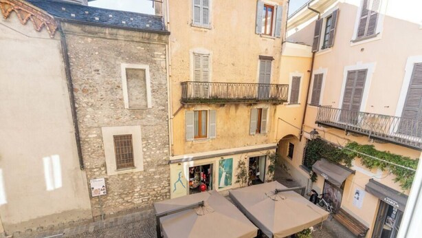 A narrow alleyway with buildings on either side, a small outdoor seating area with tables and umbrellas, and a visible storefront with a sign. - SANTA MARTA by Design Studio (Bellano)