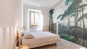 A bedroom with a bed, a window, a wall-mounted lamp, and a painting of trees. - SANTA MARTA by Design Studio (Bellano)