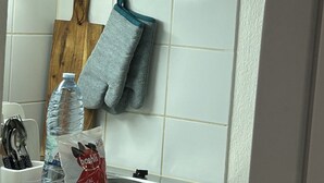 Una cocina con azulejos blancos, una tabla de cortar de madera, una tetera, una botella de agua y un paquete de mini café soluble.