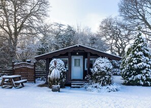 A wooden cabin with a snow-covered entrance, a bench, and a snow-covered tree in the foreground. - 0 bedroom accommodation in Brecon Beacons National Park, (Brecon Beacons National Park,)