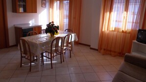 Ein Essbereich mit einem für sechs Personen gedeckten Tisch, umgeben von Holzstühlen. Links befindet sich ein Schrank mit Glastüren, rechts ein Fernseher auf einem Schrank.
