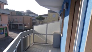 Ein Balkon mit Fliesenboden, einer weißen Bank und Blick auf die Straße sowie die umliegenden Gebäude.