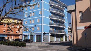 Ein mehrstöckiges Gebäude mit blauer Fassade, mehreren Balkonen und Geschäften im Erdgeschoss.
