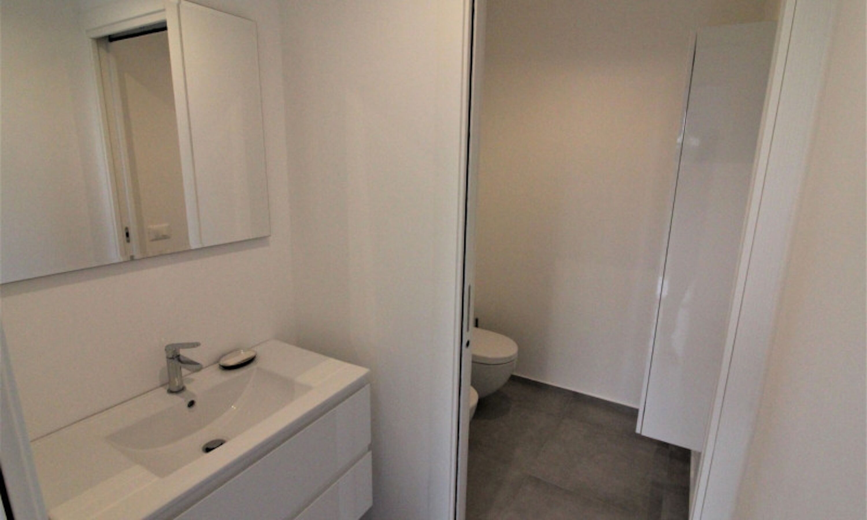 A bathroom with a white sink, mirror, and toilet.