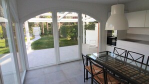 A modern kitchen with a glass dining table, white cabinets, and a view of a garden. - Modern villa a few steps from the beach (Lignano Sabbiadoro)