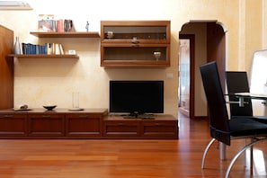 A living room with a flat-screen TV, wooden cabinets, a glass table, and a black chair. - Lucy’s House: Comfort and Relaxation in Livorno (Livorno)