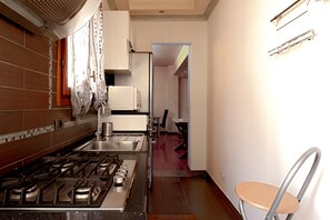 A kitchen with a gas stove, a sink, and cabinets. There is a chair and a table in the adjacent dining area. - Lucy’s House: Comfort and Relaxation in Livorno (Livorno)