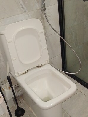 A toilet with a shower attachment in a bathroom with tiled walls and floor. - Cozy 1-bedroom apartment in serene Nairobi with fitness room Lavington-Kilimani (Nairobi)