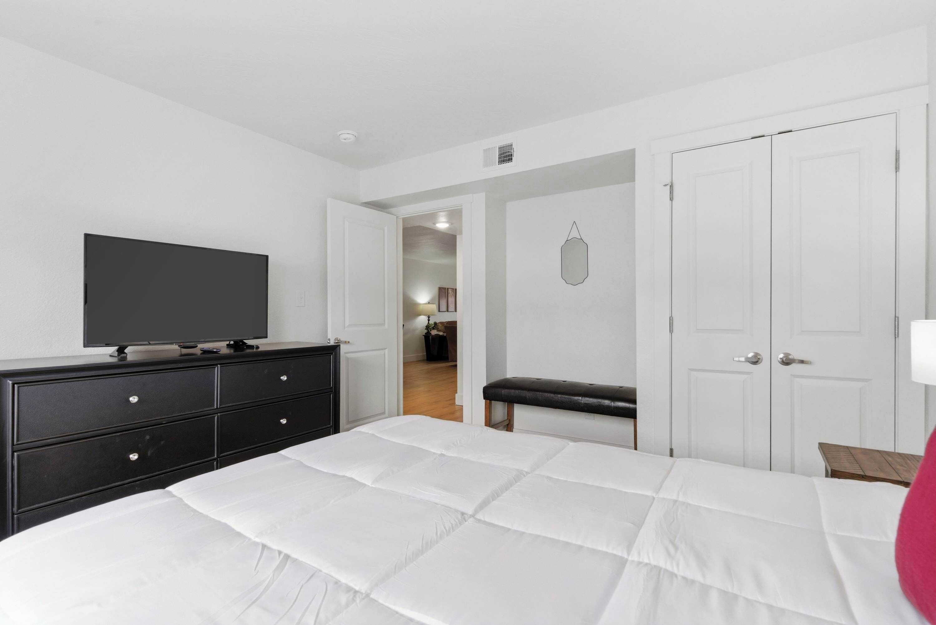 A bedroom with a bed, a dresser, a television, a bench, and a wardrobe.